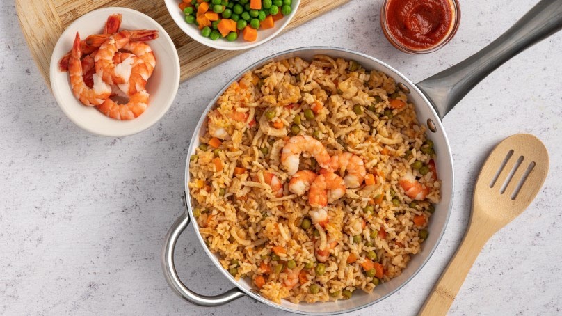 Shrimp Fried Rice, stainless steel pot, wooden spoon, cocktail sauce, shrimp, mixed veggies, cutting boatrd, stone countertop