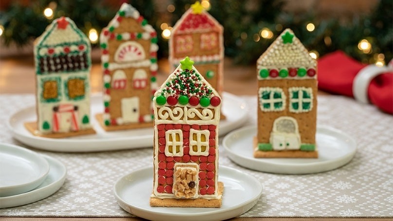 Easy Honey Made Holiday Houses on white plates, red napkin, woven placemat, holiday garland with white lights, wood tabletop