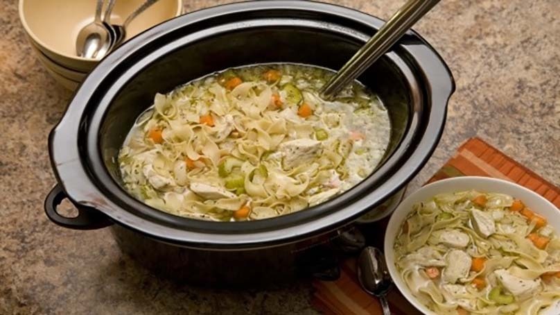 Slow Cooker Chicken Noodle Soup, bowl of soup, crockpot full of soup, empty bowls and spoons, placemat, stone countertop