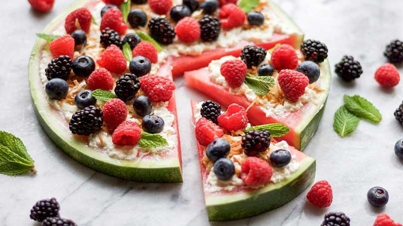 Watermelon dessert pizza with fresh berries on top with mint leaf garnish, white stone countertop