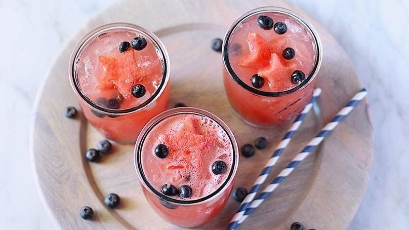 Watermelon infused lemonade with fresh blueberries, blue and white striped straws, white stone countertop